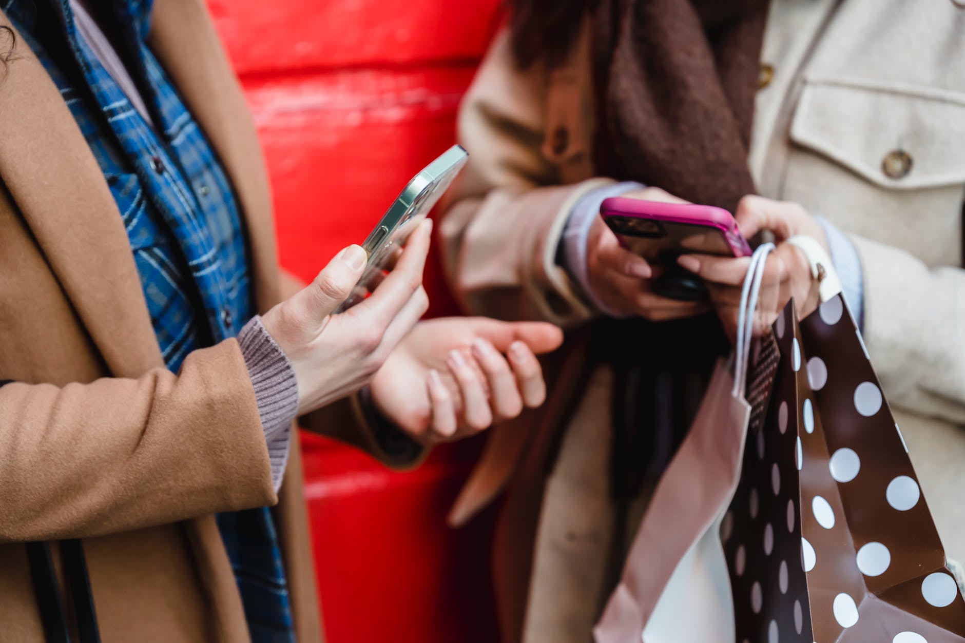unrecognizable women messaging on smartphones after shopping in city